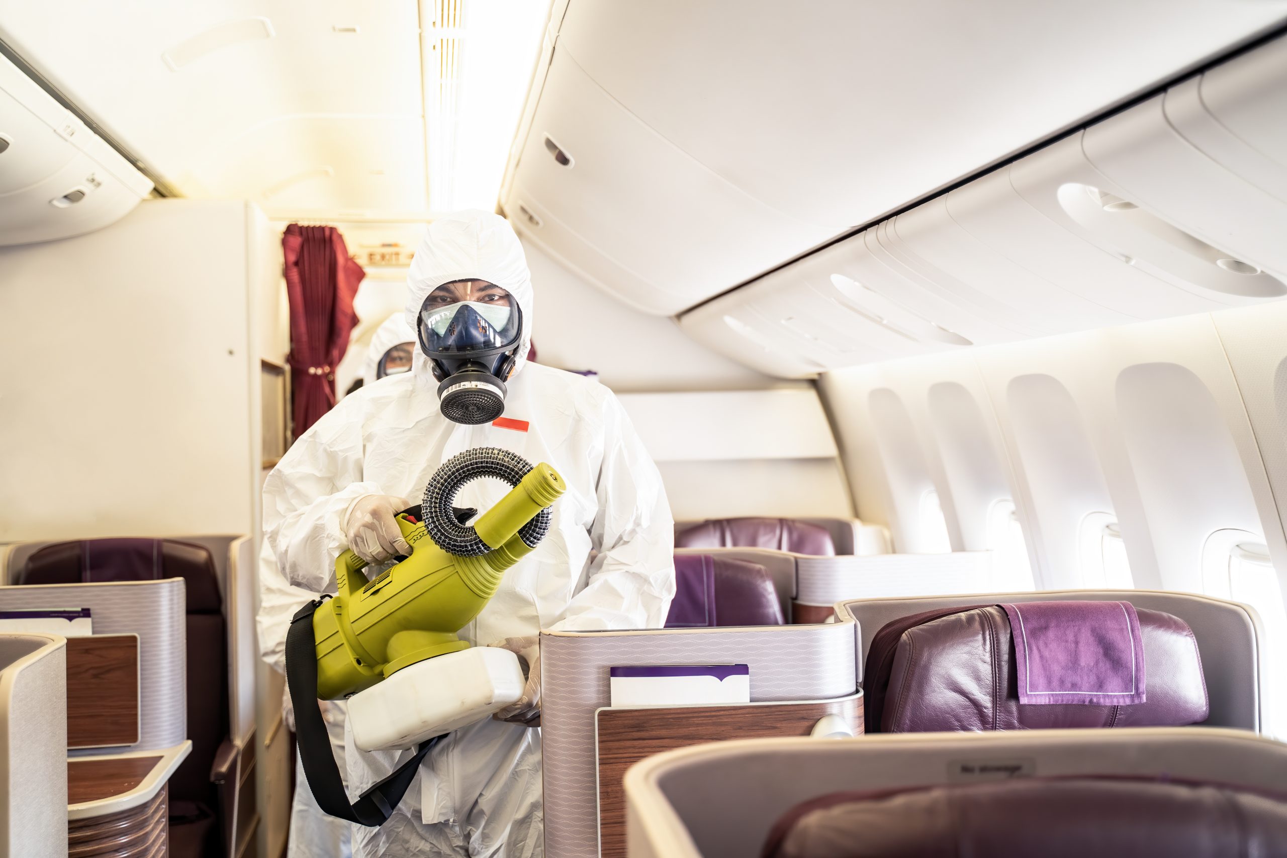 Cleaner officers hold cleaning device on airplane passenger cabin. An employee sprays disinfectant aboard a plane, during airline's sanitary measures to help curb the spread of Coronavirus pandemic.